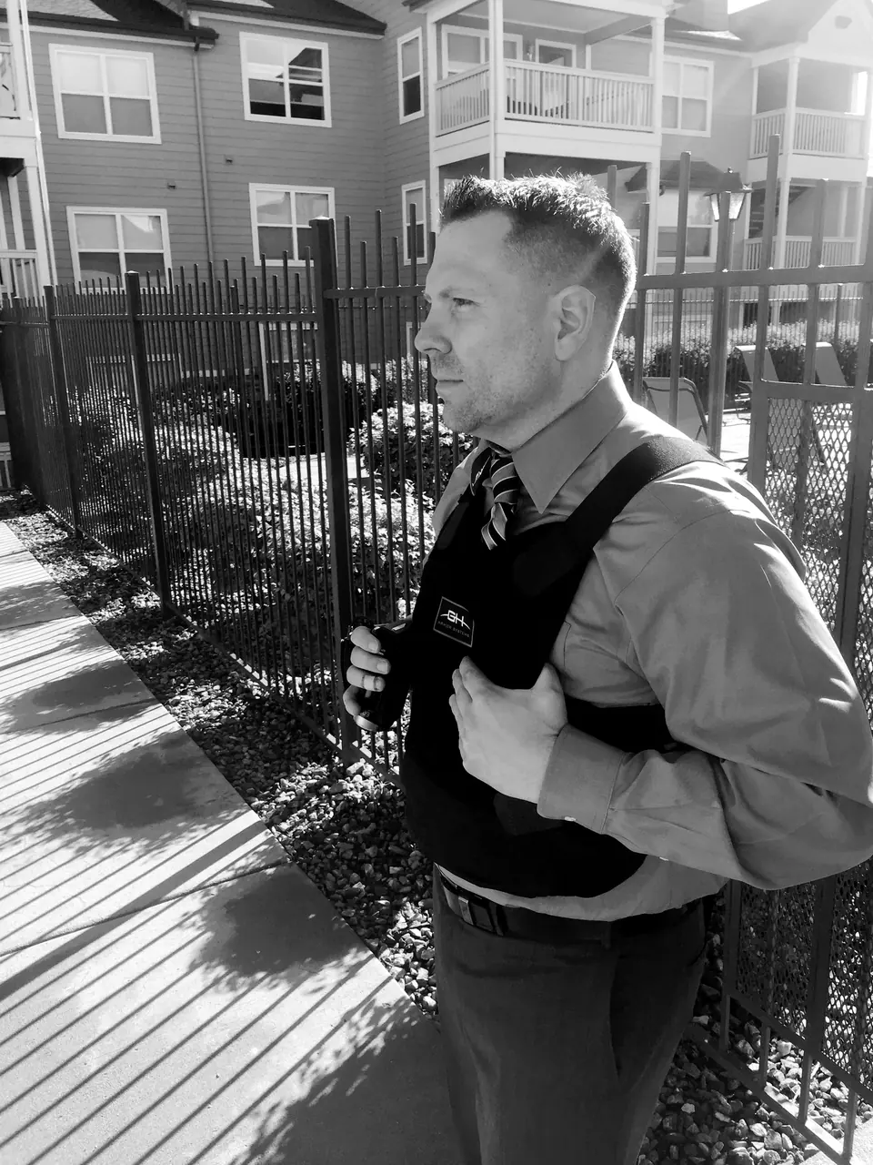 Craig Smith in a shirt, tie and body-armor vest beside an iron fence