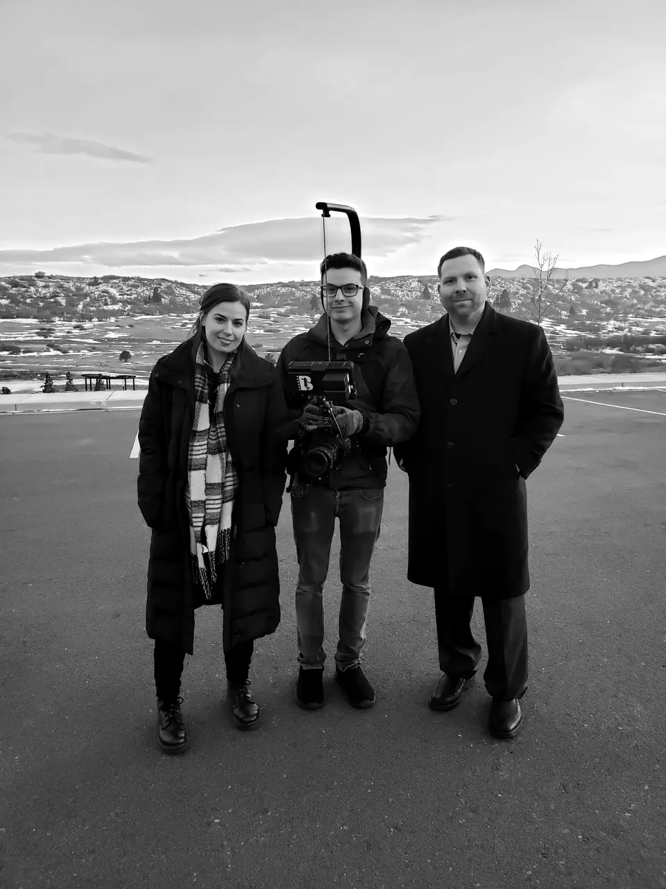 Craig Smith standing outdoors with a two-person film crew, mountains behind them