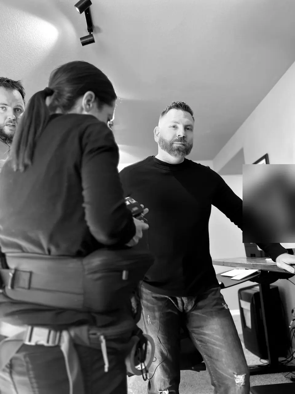 Craig Smith standing at his desk while a crew member prepares equipment during a filmed interview; monitor obscured