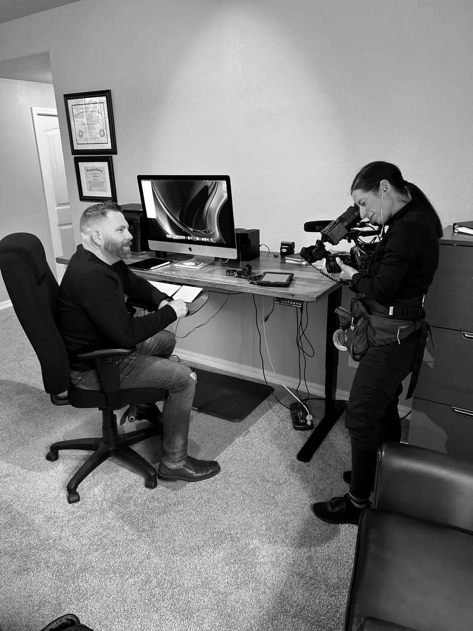 Craig Smith seated at his desk while a camera operator films