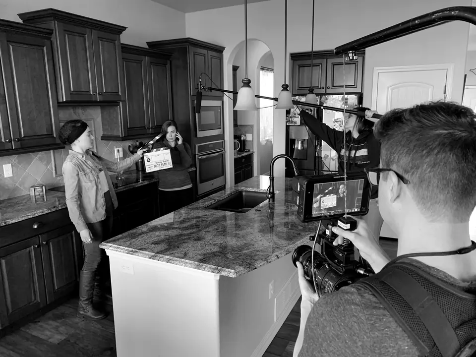 A film crew shooting a scene in a kitchen, with a clapperboard